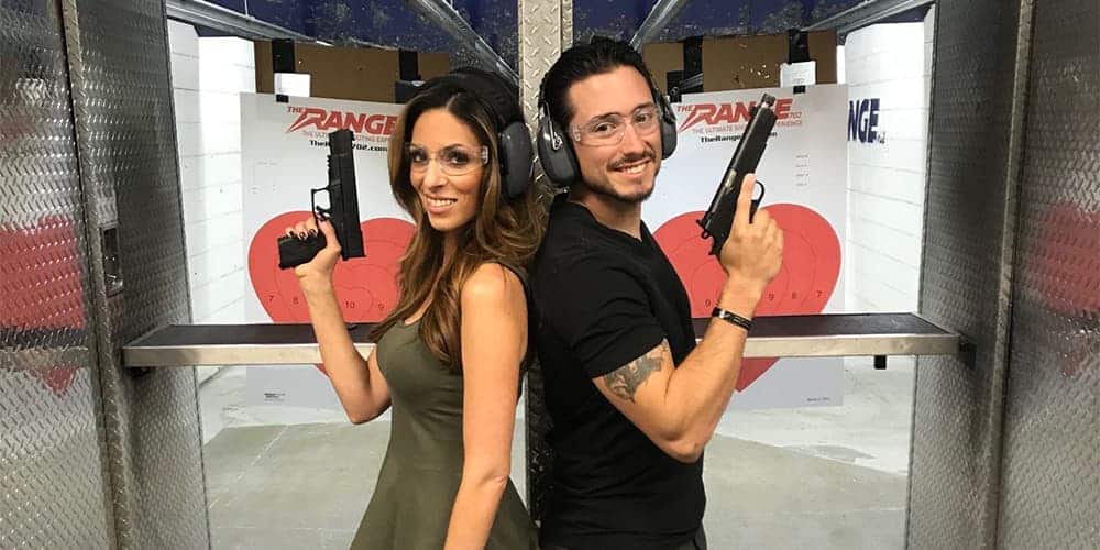 lady and man standing back to back in front of shooting range holding m1911 pistols