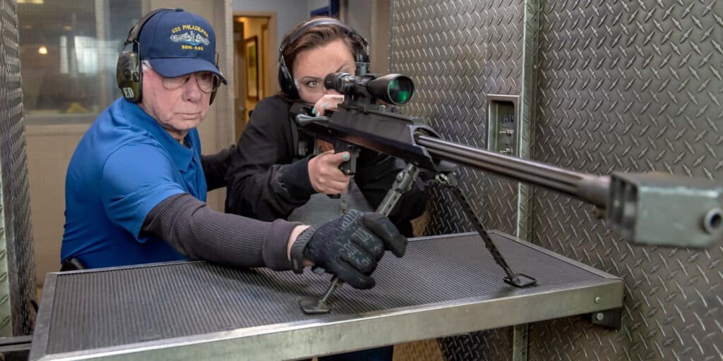 man holding stand of 50 cal while woman shoots the gun