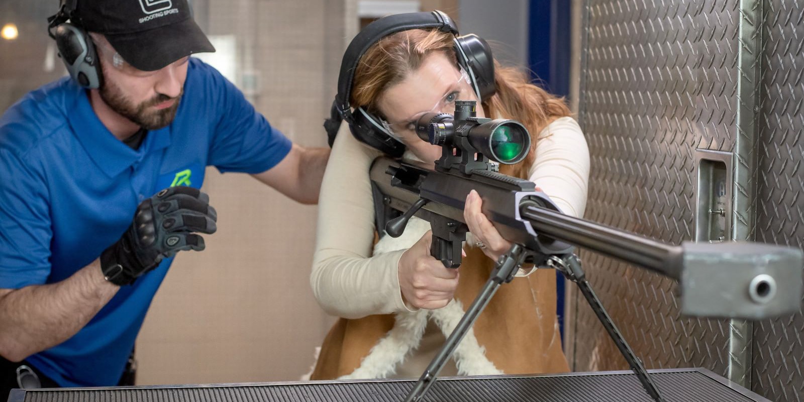 trainer standing behind women firing a 50 cal gun