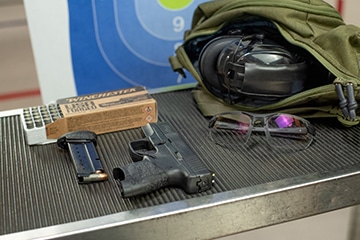 handgun laying on a shooting stand next to protective gear